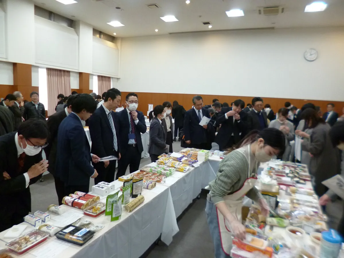ねり製品が並ぶ会場。長机に並んだかまぼこなどのねり製品を、スーツ姿の来場者がのぞき込むようにして見ている。